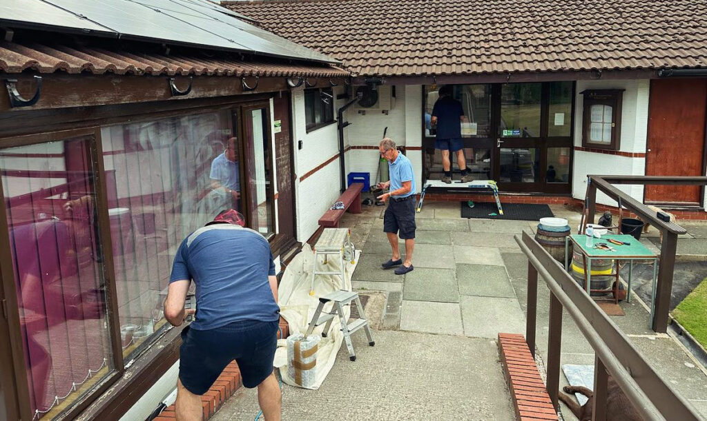 People working on the outside of the clubhouse, painting and repairing.